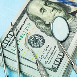 dental instruments lying on top of a stack of hundred-dollar bills 