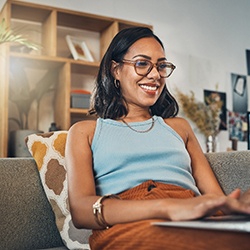 Woman with glasses sitting on couch and typing on laptop