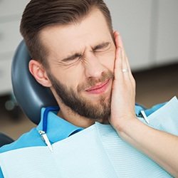 Man in dental chair holding cheek