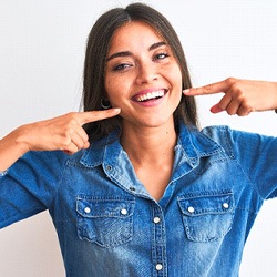 Woman pointing at her teeth, enjoying benefits of veneers