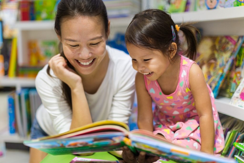 Parent and child reading book together in library